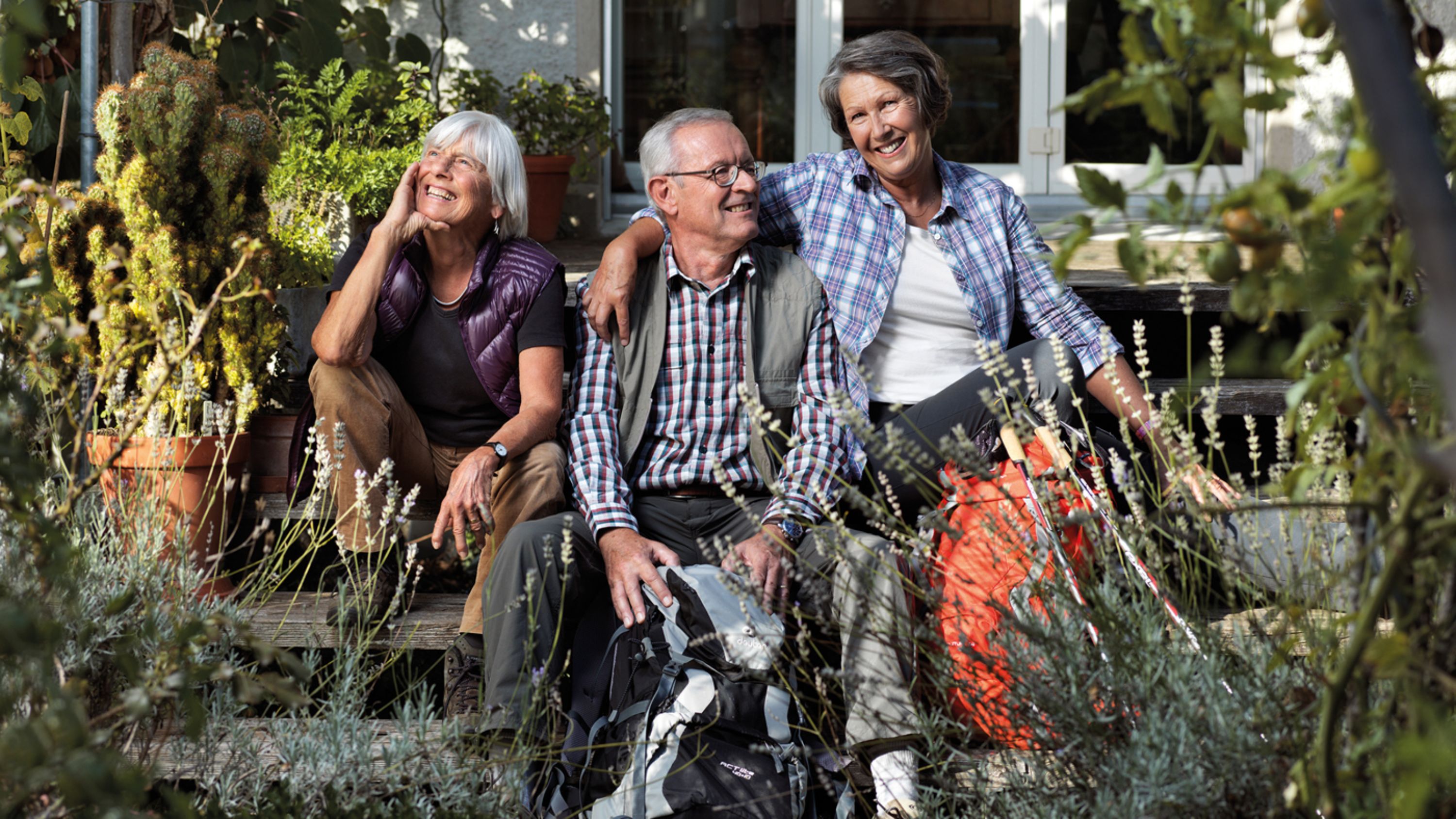 Drei ältere Menschen sitzen auf dem Treppen im Garten und lachen